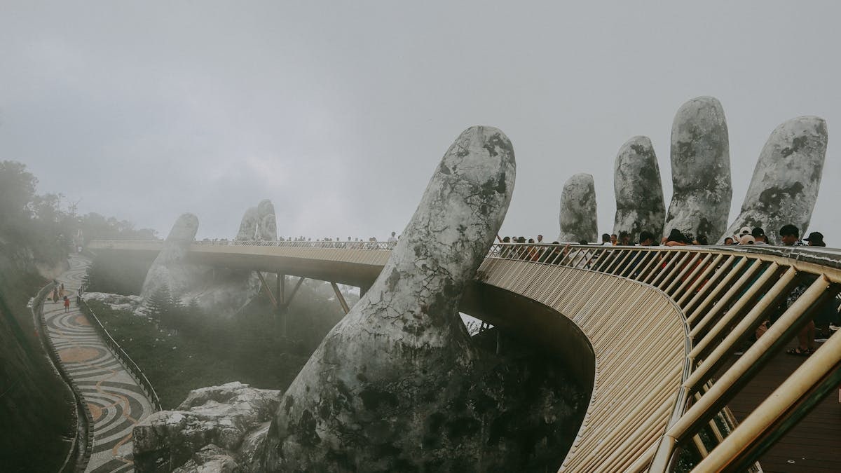 Stunning view of Golden Bridge held by stone hands enveloped in mist, Ba Na Hills.