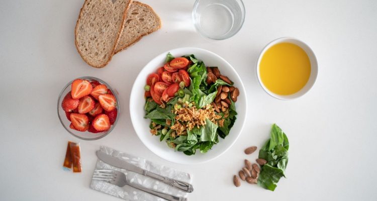 Top view of a healthy salad and fresh ingredients with bread and juice on a white surface.