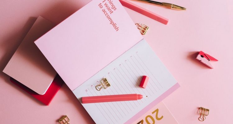 Organized workspace with pink planner, pen, and clips on pastel background.